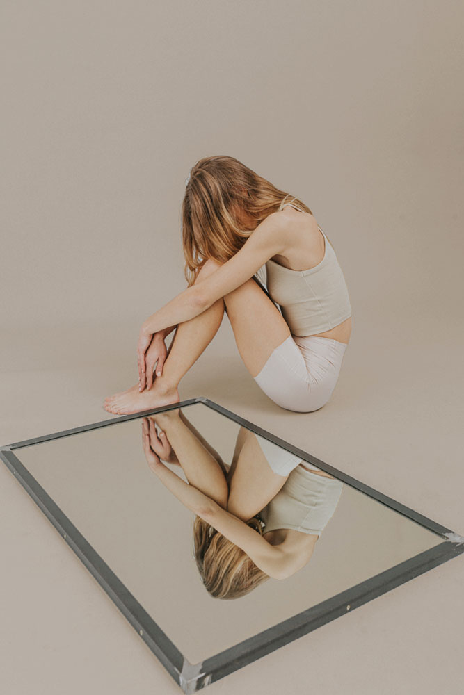 Una mujer en una postura de recogimiento, frente a su reflejo